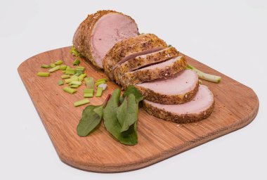 Baharatlı domuz filetosu, ahşap kesim tahtasına yeşil soğan ve bitkilerle yakın plan. Yemek tarifleri ve restoran menüsü için mükemmel ev yapımı yemekler.