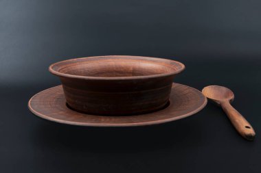 Çamur tabağı seramik kâse ve ahşap kaşıkla siyah arka plan kırsal mutfak gereçlerine konulmuş geleneksel el yapımı çömlek ve doğal malzeme konsepti.