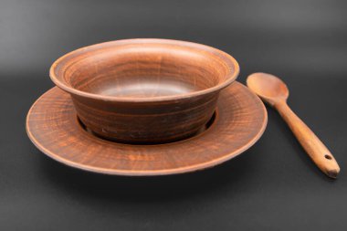 Çamur tabağı seramik kâse ve ahşap kaşıkla siyah arka plan kırsal mutfak gereçlerine konulmuş geleneksel el yapımı çömlek ve doğal malzeme konsepti.