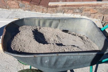 Açık hava inşaatında kuru çimento dolu metal el arabası. İnşaat malzemeleri, yenileme işleri, DIY projeleri ve inşaat mühendisliği kavramı.
