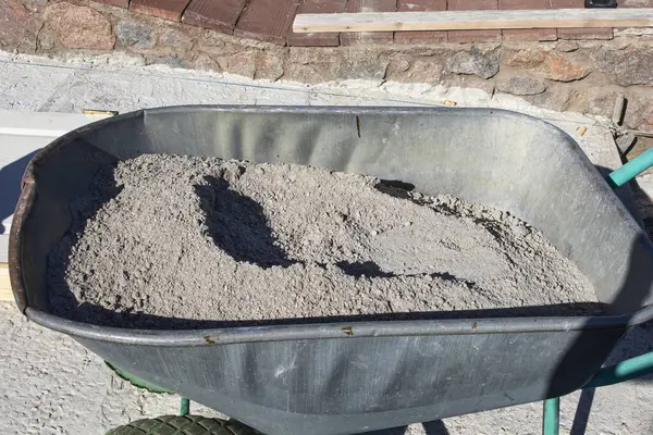 Açık hava inşaatında kuru çimento dolu metal el arabası. İnşaat malzemeleri, yenileme işleri, DIY projeleri ve inşaat mühendisliği kavramı.