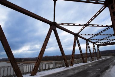 Paslı metal köprünün atmosferik görüntüsü geometrik yapı ve çarpıcı bulutlu gökyüzünün altında çatlak asfalt yol. Sanayi mirası, mimarisi ve mühendisliği kavramı.