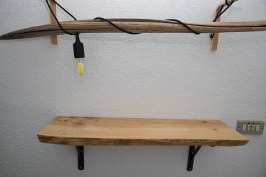 Ampul ve kabloyla beyaz desenli duvara sabitlenmiş ahşap rafı kapat. Minimalist iç tasarım, el yapımı doğal malzemeler ve kırsal ev dekorasyonu kavramı..
