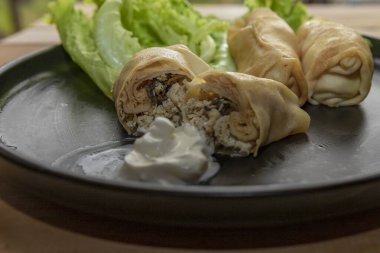 Ev yapımı doldurulmuş, içi et dolu, taze marul yapraklı, soğan halkaları ve siyah tabakta ekşi krema ile servis edilen gözlemeleri kapatın. Geleneksel Slav mutfağı ve ev yapımı yemekler.