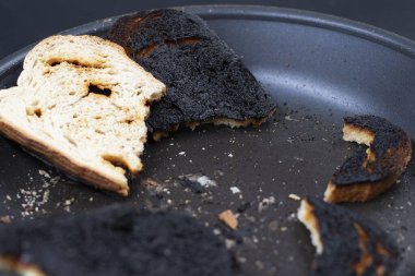 Siyah arka planda kızarmış tavada yanmış ekmek dilimlerinin yakın çekimi. Pişirme hatası, yanmış yemek, mutfakta hata ve yiyecek israfı kavramı..