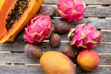 Papaya, ejderha meyvesi, dikenli armut ve kırsal bir ahşap masa üzerindeki mango da dahil olmak üzere çeşitli egzotik meyvelerin üst görüntüsü. Sağlıklı beslenme, organik gıda, yaz ve tropikal yaşam tarzı kavramı.