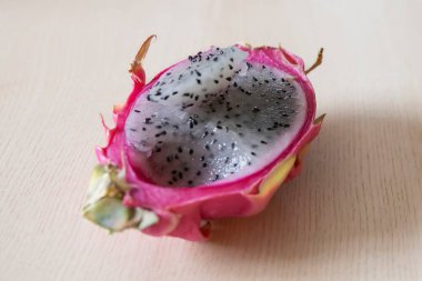 Taze ejderha meyvesi (pitaya), sulu beyaz hamurlu ve ahşap zemin üzerinde siyah tohumlu yakın plan. Sağlıklı beslenmeyi, vejetaryen beslenmeyi ve organik beslenmeyi sembolize eden egzotik tropikal meyve..