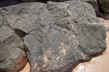 Doğal çatlaklara, kaba dokulara ve kum izlerine sahip koyu volkanik kayalara yakın çekim. Jeoloji kavramı, doğal arka plan, taş dokusu ve engebeli kıyı manzarası..