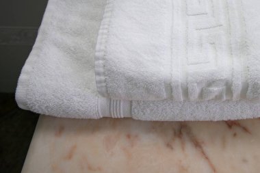 Temiz beyaz pamuk havluları mermer bir tezgahın üzerine güzelce katlanmış. Hijyen, banyo dekorasyonu, spa, lüks otel ve konfor kavramı..
