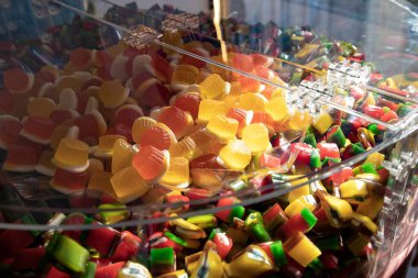 Close up of assorted gummy candies in bright yellow, red, green, and orange colors displayed in a transparent bulk container. Sweet confectionery background, candy shop, and dessert concept.
