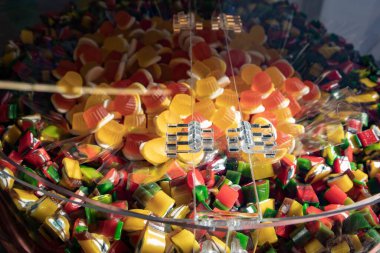 Close up of assorted gummy candies in bright yellow, red, green, and orange colors displayed in a transparent bulk container. Sweet confectionery background, candy shop, and dessert concept.