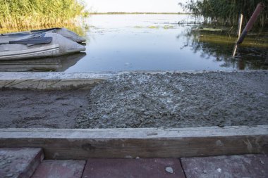 Nehir kıyısına dökülen taze ıslak betonu şişirilebilir tekne ve yeşil sazlıklarla kapatın. İnşaat, rıhtım inşaatı, rıhtım, inşaat mühendisliği ve açık hava yaşam tarzı kavramı