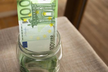 Cam kavanoza yerleştirilmiş 100 avroya yakın banknot. Kişisel tasarruf, yatırım, mali güvenlik, mevduat ve para yönetimi kavramı.