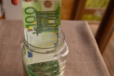 100 Euro 'luk banknotu cam bir kavanoza koymak. Tasarruf, mali planlama, yatırım ve kişisel finans yönetimi kavramı.