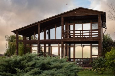 Modern eco wooden house with glass facade surrounded by plants and evening light reflections. Concept of sustainable architecture and nature harmony.