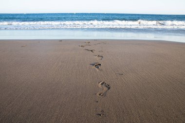 Okyanusa giden volkanik kumdaki ayak izleri Tenerife Kanarya Adaları İspanya seyahat ve rahatlama için huzurlu deniz manzarası