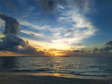 Gün batımı mavi gökyüzü ve okyanusta kara bulutlar ufukta küçük Maldivler adaları. Tropik bir cennette yaz tatili. Sessiz renklerle güzel bir deniz manzarası. Huzur ve rahatlama.