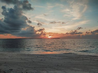Okyanusta güzel bir gün batımı ve ufukta küçük adalar. Tropik cennet, Maldivler. Yaz tatili, huzur ve rahatlama. Sönük kırmızı renkte güzel bir deniz manzarası.