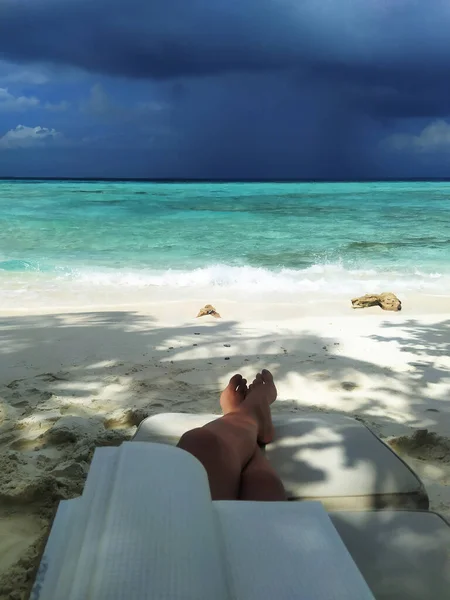 Legs of a woman resting with notepad on a sunbed by the ocean. A beach with the white sand. Maldives, tropical paradise. Summer vacation. Beautiful sea view. Inspiration, freelancing, remote work.