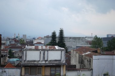 Yıpranmış çatıları, eski binaları ve bulutlu bir gökyüzünün altındaki uzak dağları olan şehir silueti. Bu şehir manzarası kırsal cazibeyi, dokulu mimariyi ve yazı işleri ve seyahat içeriği için mükemmel nostaljik havayı yakalar..