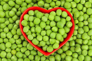 Arka plan olarak kırmızı seramik kasede taze yeşil bezelyeler. Üst Manzara. Düz yatıyordu.