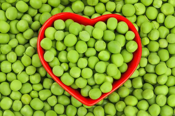 Arka plan olarak kırmızı seramik kasede taze yeşil bezelyeler. Üst Manzara. Düz yatıyordu.