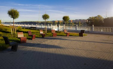 Yeşil şehir kıyısı manzaralı asfalt sokak bölgesi ve dinlenmek için ahşap, modern rahat sandalyeler sabah güneşinin doğuşunu gösteren uzay fotoğrafları.