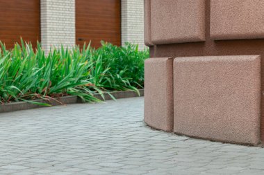 Dış yapı tasarımı, duvarın yakın elementi tuğla bej rengi, kaldırım elementi çimen çiçek yatağı ve garaj alanı ile desenli, arka plan bulanık, şehir alanı temiz.