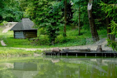 country side summer time landscape of water reservoir wooden pier with small fishing boat and rustic rural house village environment clipart