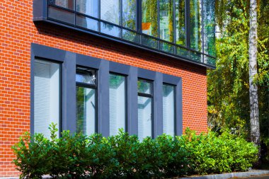 office building exterior facade windows reflection and red brick wall frame outside green city landmark view with bush plants and tree clipart