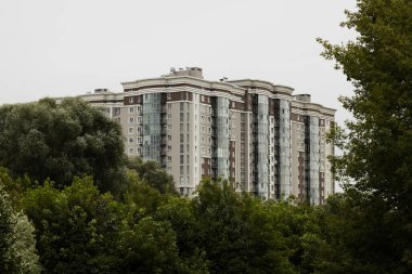 Çok katlı çok katlı büyük bina dış duvarlar ve pencereler bulutlu hava parkı bölgesi ağaçları yeşil yeşil yeşil gökyüzü arkaplanı