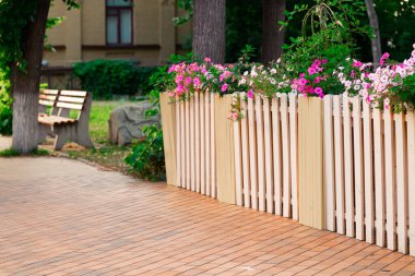 Ilık, aydınlık manzara kare park alanı yayaya ait patika çiçek tarhı ve dekoratif çit boyunca ilerliyor.