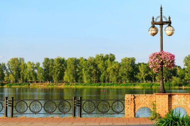 Rıhtım manzaralı fener çiçek saksısı asıyor nehir suyu boyunca yatay manzara açık hava saatinde yeşil park resimli arka plan