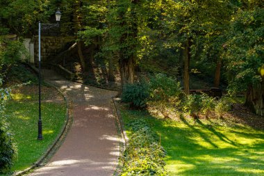 spring bright day seasonal nature scenic view landscaped park paved track lantern and green grass lawn hills under vivid yellow sun light