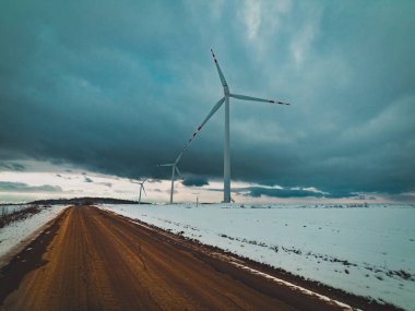 Arka planda yel değirmenleri olan karlı tarlalar arasındaki yol