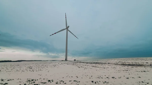 Arkasında bulutlu bir gökyüzü olan karlı bir tarlada yel değirmeni