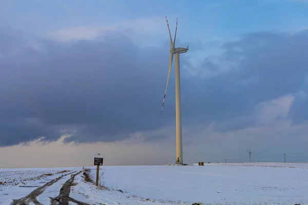 Arkasında bulutlu bir gökyüzü olan karlı bir tarlada yel değirmeni