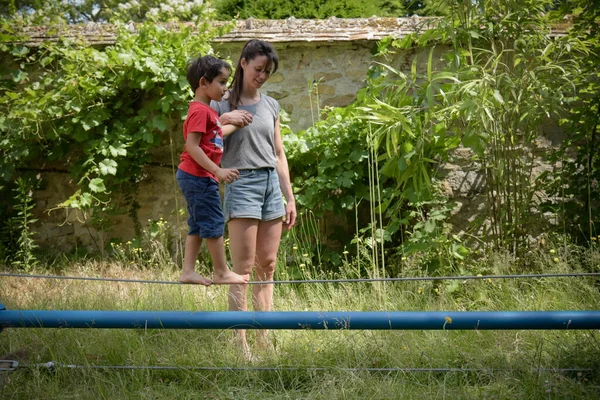 在一位女教练的帮助下 小男孩在一座花园里走钢丝 — 图库照片