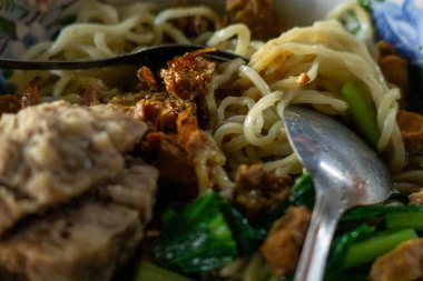 Mie Ayam Bakso 'nun yakın çekimi, tavuk, köfte, yeşil sebze ve kızarmış arpacık soğanlı Endonezya eriştesi. Lezzetli tatların ve dokuların hoş bir karışımı canlı mavi bir masada..