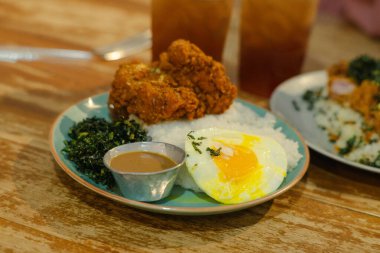 Kızarmış tavuk, kabarık pilav, güneşli bir yumurta, sotelenmiş yeşillikler ve mükemmel lezzet dengesi için ferahlatıcı buzlu çayın yanında sunulan bol soslu bir yemek..
