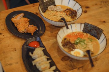 Ağız sulandırıcı, lezzetli ramen kaseleri çıtır tonkatsu ve mükemmel buharda pişirilmiş gyoza ile eşleştirilmiş. Japon mutfağının rahatlatıcı ve otantik tadı kırsal ahşap bir masada servis edilir..
