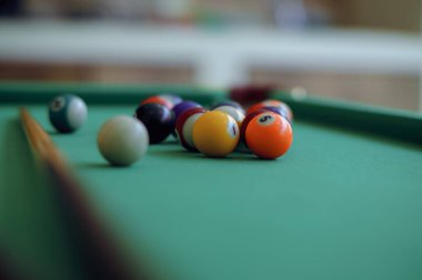 Klasik yeşil bilardo masası. Rengarenk toplarla dolu, oynamaya hazır. Masanın üzerinde duran iki tahta işaret oyunun zarif ve rekabetçi atmosferini güçlendiriyor..