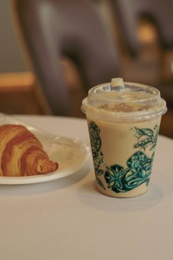 Sıcak bir buzlu kahve, yeşil çay ve beyaz bir masada taze kruvasan. Rahatlatıcı bir kafe anı için mükemmel..