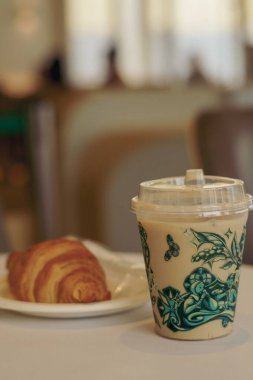 Sıcak bir buzlu kahve, yeşil çay ve beyaz bir masada taze kruvasan. Rahatlatıcı bir kafe anı için mükemmel..