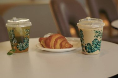 Sıcak bir buzlu kahve, yeşil çay ve beyaz bir masada taze kruvasan. Rahatlatıcı bir kafe anı için mükemmel..