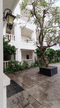 Koloni tarzı otel avlusu tropikal bitkiler, beyaz sütunlar, klasik lambalar, ve asfalt zemin, dingin ve zarif tatil atmosferleri çağrıştırıyor..