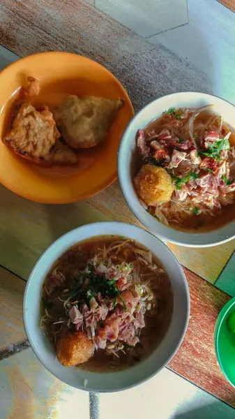 İçten bir kase geleneksel soto dilimlenmiş tavuk, fasulye filizi ve lenthok ile renkli bir masada kızarmış atıştırmalıklarla servis edilir..