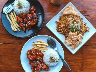 Baharatlı susamlı tavuk, pilav ve patates kızartması. Lezzetli erişte ve çıtır krakerle birlikte. Mükemmel yemek fotoğrafçılığı için kırsal ahşap sofra takımında servis ediliyor..