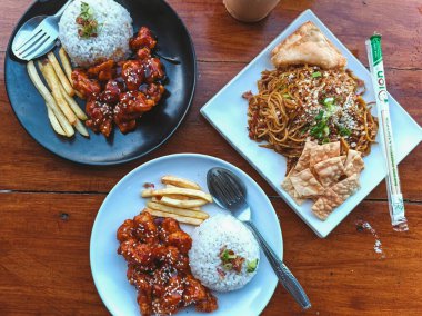 Baharatlı susamlı tavuk, pilav ve patates kızartması. Lezzetli erişte ve çıtır krakerle birlikte. Mükemmel yemek fotoğrafçılığı için kırsal ahşap sofra takımında servis ediliyor..