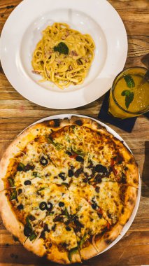 Sıcak bir kafede servis edilen ferahlatıcı bir narenciye ile eşleştirilmiş, peynirli sığır etli pizza ve kremalı makarna..